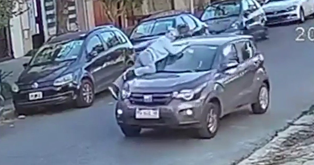 Mujer colgada del capot de un auto en una calle de Ramos Mejía