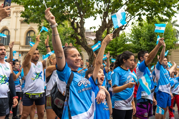 Personas corriendo en una carrera callejera con remeras celestes y blancas