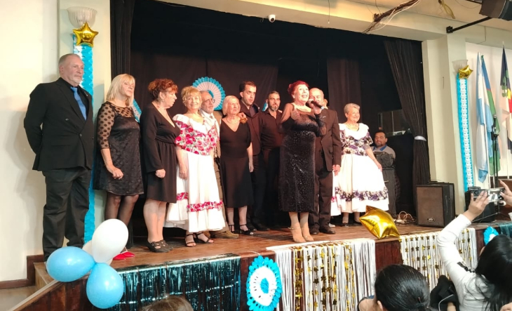 Personas reunidas en un salón con banderas argentinas y comida tradicional
