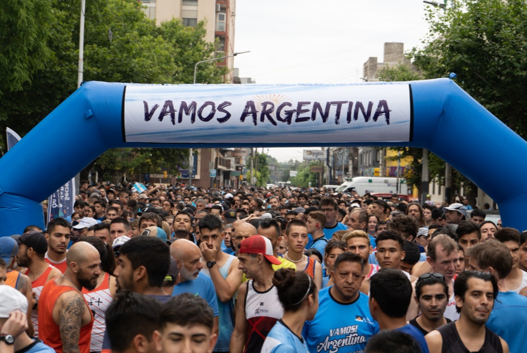 Personas corriendo en una carrera callejera con remeras celestes y blancas