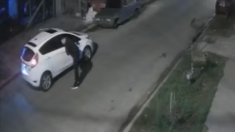 Calle residencial con autos estacionados y una cámara de seguridad en un poste