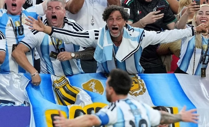 Lionel Messi celebra un gol con los brazos abiertos frente a una bandera de Villa Unión y Almirante Brown