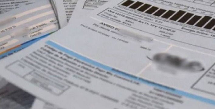 Boletas de luz, gas y agua sobre una mesa junto a billetes de pesos